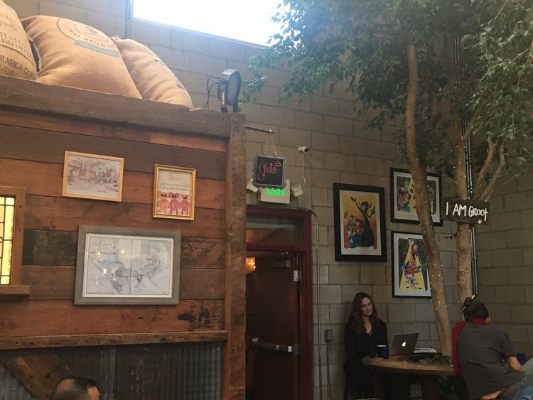 A cozy coffee shop with a tree and a wall adorned with pictures. A perfect spot to relax and enjoy a cup of coffee.