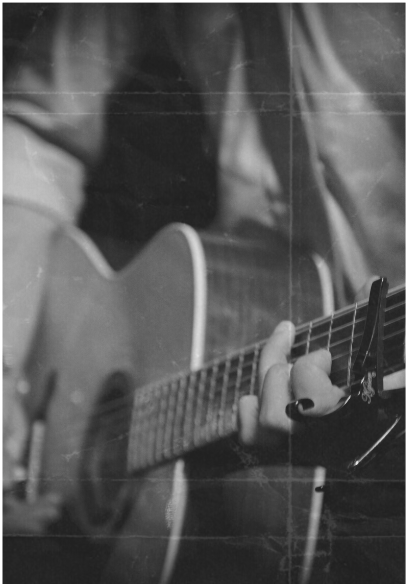 A person strumming an acoustic guitar in a black and white photo.