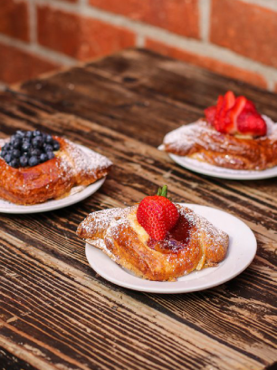 Three delicious and flaky fruit danish on small plates filled with a sweet and tart fruit filling available in Republic of Pie.