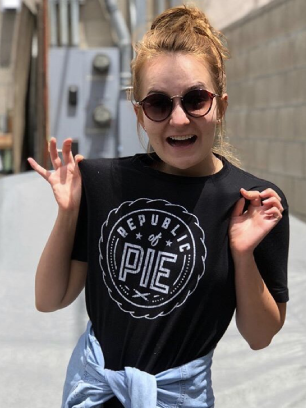 A girl wearing a black shirt with the words "Restaurant of Pie" on it, ROP merch.