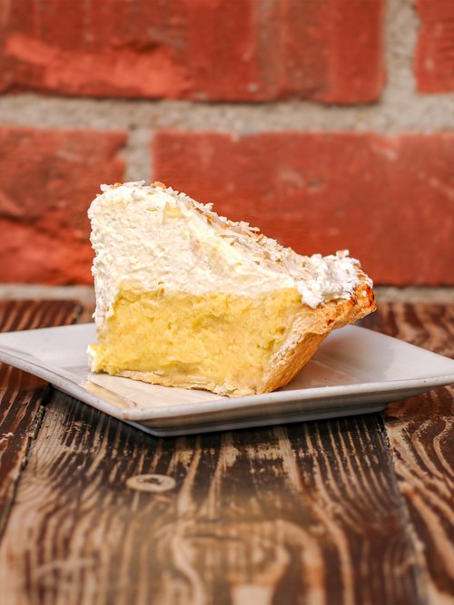 Savor the temptation of a heavenly slice of coconut cream pie, featuring a decadent custard filling nestled within a flaky crust, elegantly presented on a white plate. 