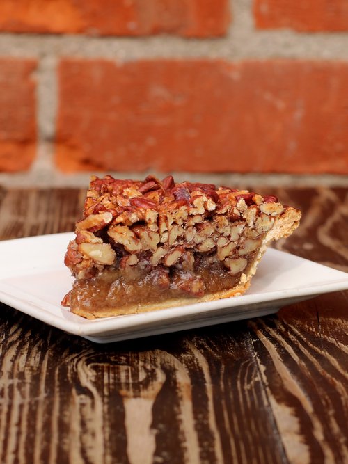 A slice of pecan pie, generously packed with an abundance of pecans that surpasses what you'll typically find in other bakeries
