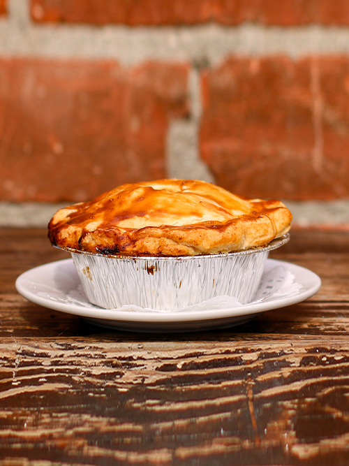 A pie on a plate with a flaky dough, placed on a wooden table.
